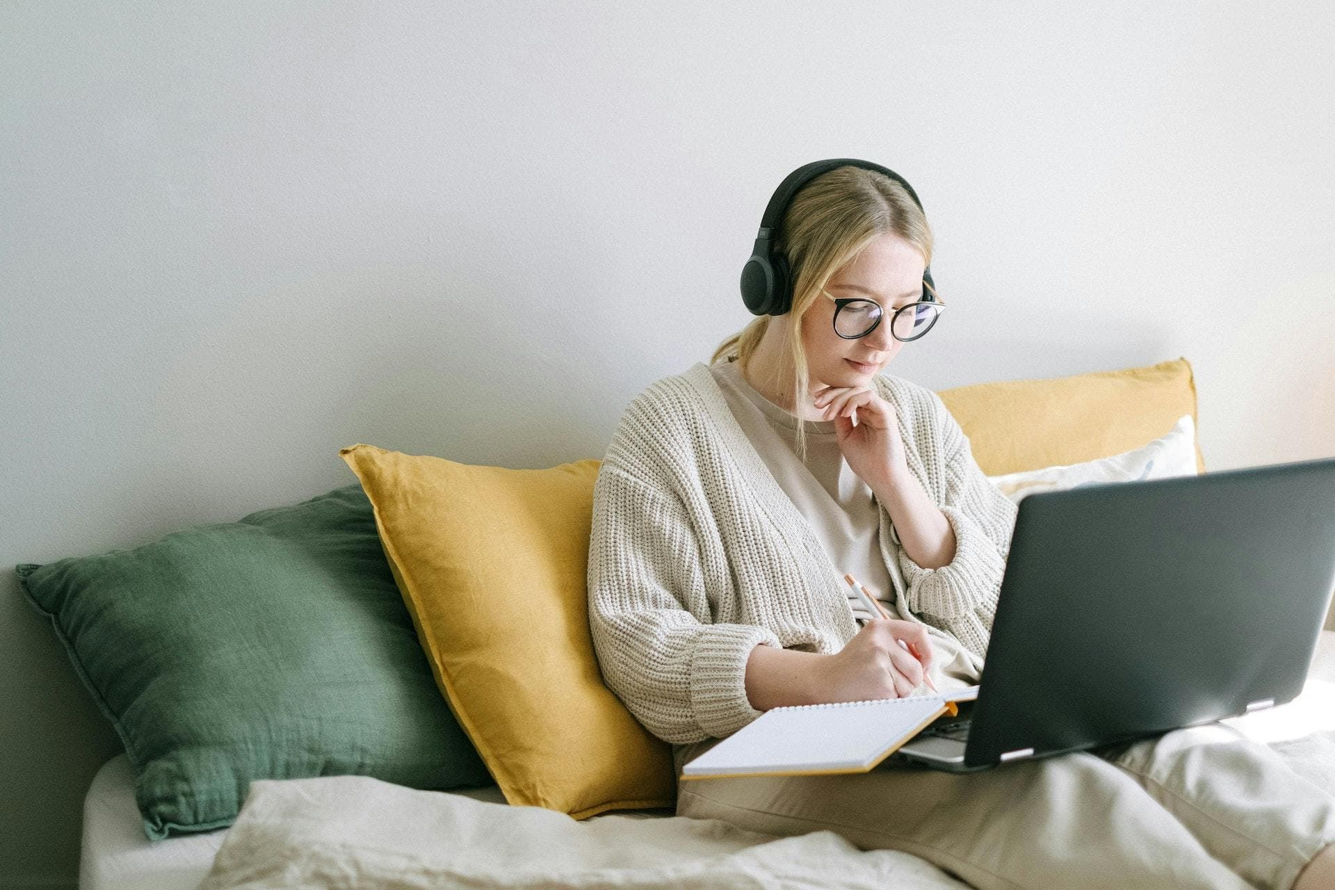 Woman wearing headphones working on laptop in bed