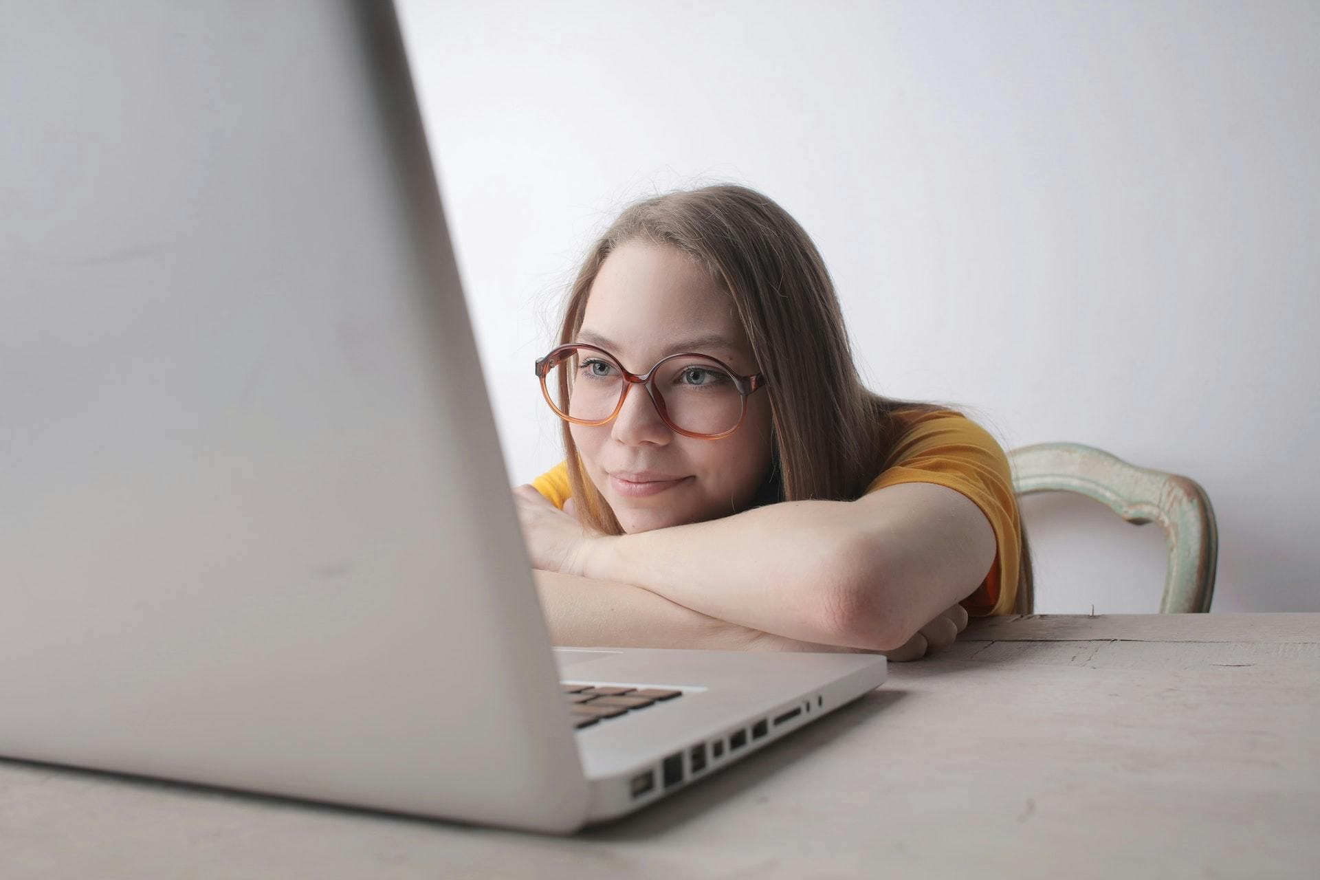 Freelancer wearing glasses leaning over desk staring at laptop and smiling