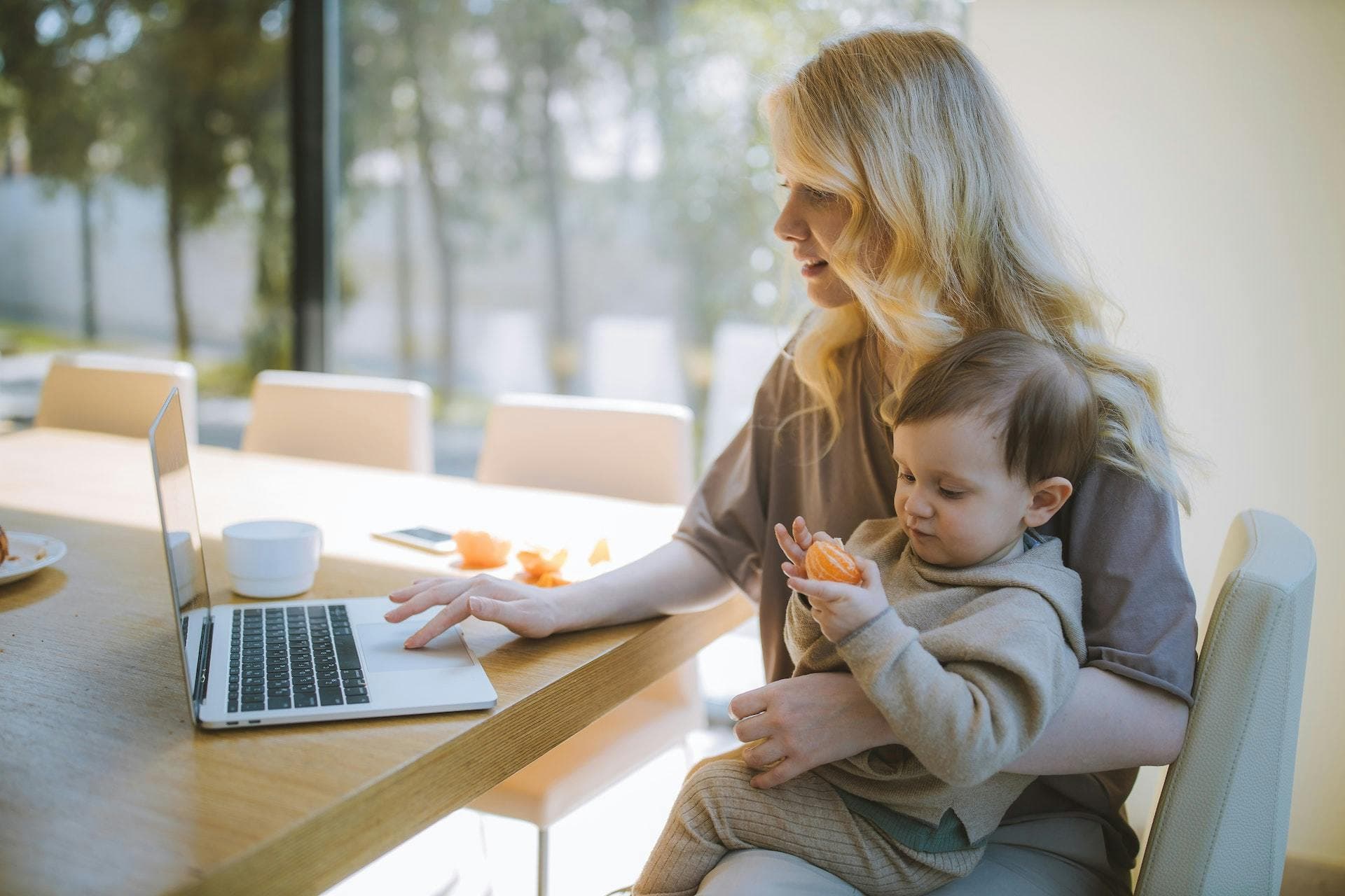 Working mother sat at laptop holding child | UK tax allowances, rates and thresholds 2023/24