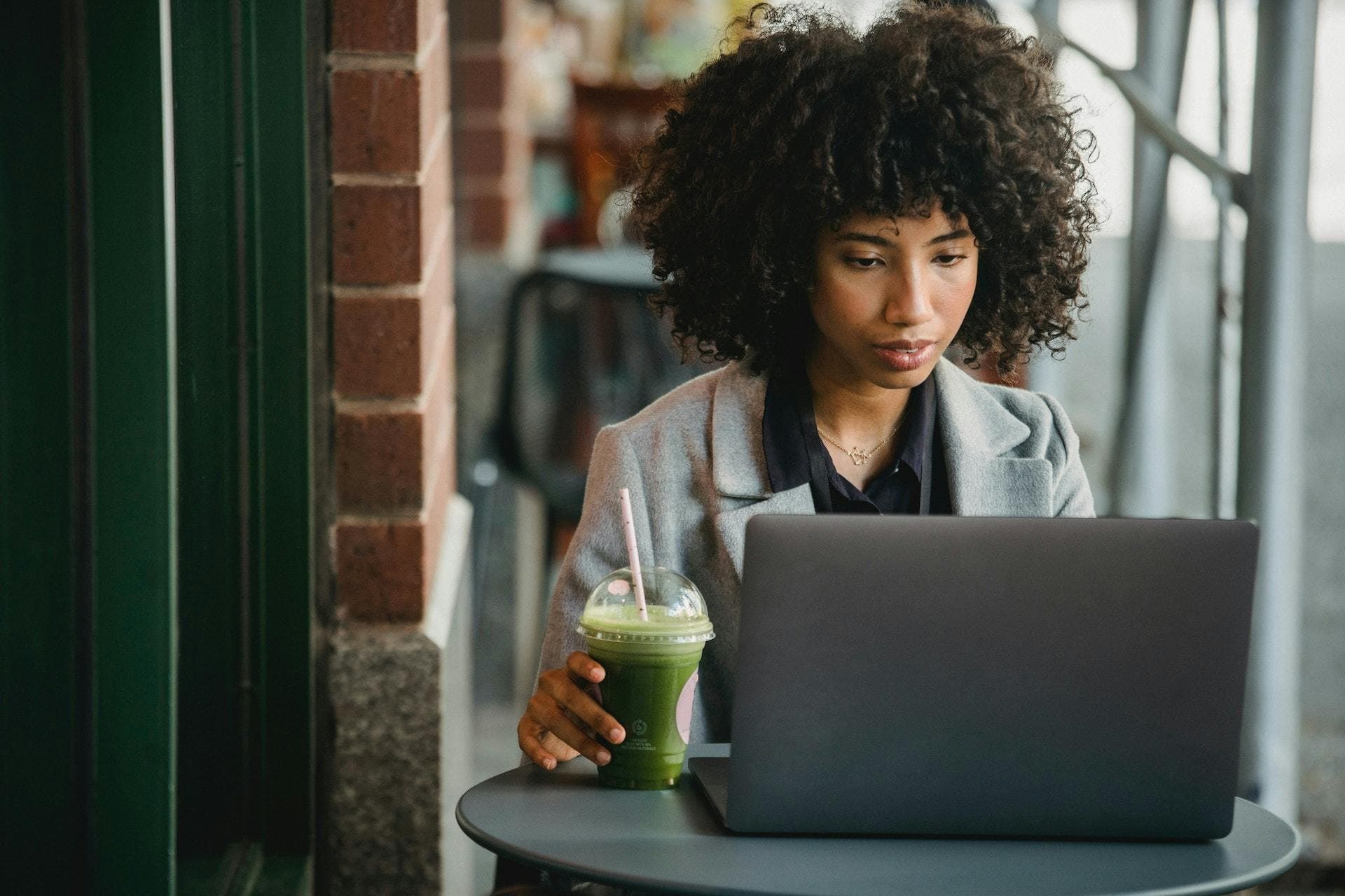 Businesswoman sat at laptop with green smoothie in hand